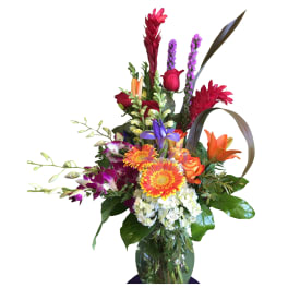 Tall mixed bouquet in a glass vase with bright tropical blooms and roses