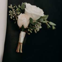 White rose boutonniere with greenery on a dark background