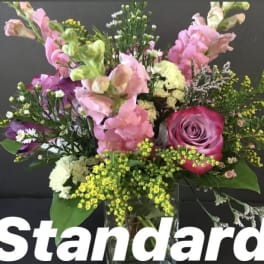 Mixed pink snapdragons and a pink rose with white and yellow accent blooms in a clear vase.