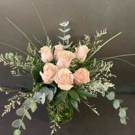 Blush pink roses in a clear glass vase with airy greenery