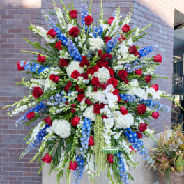 Tall standing spray with red roses, white hydrangeas and orchids, and blue delphinium on an easel