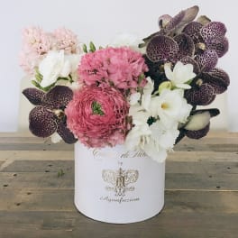 Pink and white floral arrangement in a white hatbox with dark orchids