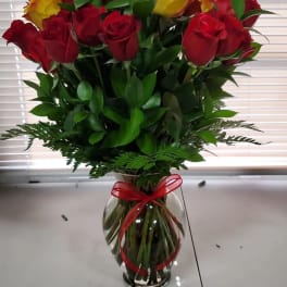 Bouquet of red and yellow roses in a clear glass vase with a red ribbon