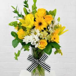 Yellow and white mixed bouquet in a glass vase with a striped ribbon