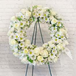 White floral wreath on a stand with roses and daisies