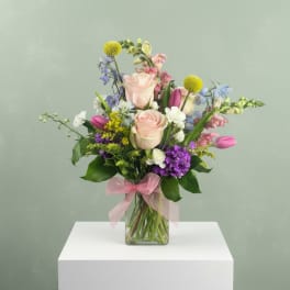 Mixed bouquet of pastel roses, tulips, and purple flowers in a glass vase