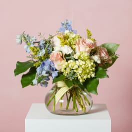 Mixed pastel bouquet in a round glass vase with a striped ribbon