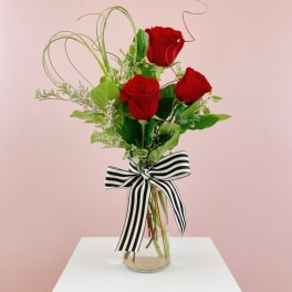 Three red roses in a glass vase with a black-and-white striped bow