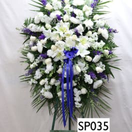 Large white and purple funeral spray on an easel with a blue ribbon
