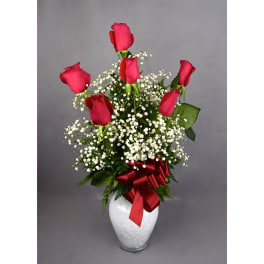 Red roses arranged in a white vase with baby's breath and a red ribbon