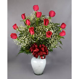 Red roses arranged in a white vase with baby's breath and a red ribbon