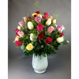 Mixed roses in pink, red, yellow, and white arranged in a white vase