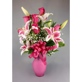 Pink roses and lilies arranged in a pink vase with a ribbon bow