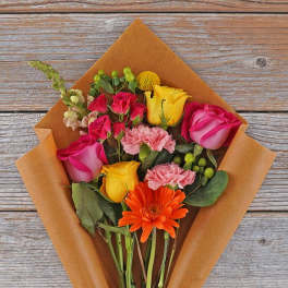 Bouquet of pink and yellow roses with an orange gerbera daisy in brown paper