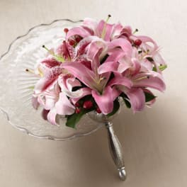 Compact bouquet of pink lilies with red berries in a silver handled holder on a glass stand