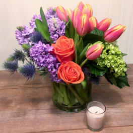 Bouquet of pink tulips, orange roses, and purple flowers in a glass vase