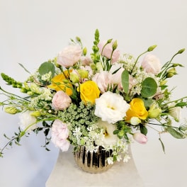 Mixed bouquet of yellow, white, and pale pink flowers in a gold vase
