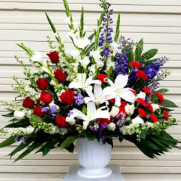 Large arrangement of red roses, white lilies, and purple flowers in a white urn