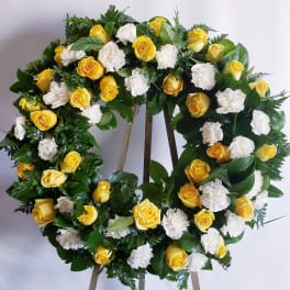 Yellow roses and white carnations arranged in a circular wreath on an easel