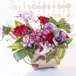 Mixed bouquet with red roses, pink orchids, and purple flowers in a woven vase