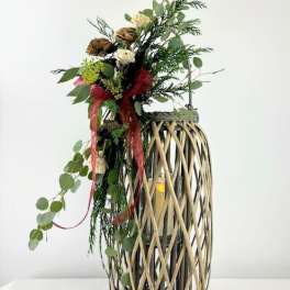 Tall floral arrangement in a woven lantern-style vase with red ribbon
