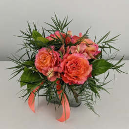 Coral roses and pink alstroemeria in a glass vase with ribbon