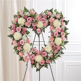 Heart-shaped floral wreath with pink roses and white blooms on a stand
