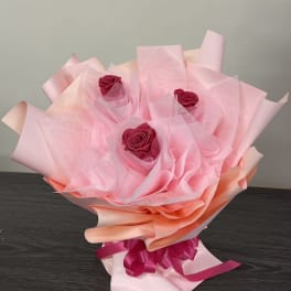 Bouquet of three pink roses wrapped in pale pink paper