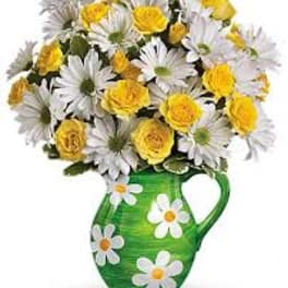 Yellow roses and white daisies in a green pitcher vase