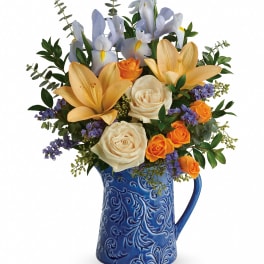 Bouquet of lilies, roses, and purple filler flowers in a blue ceramic pitcher