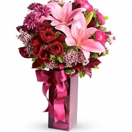 Bouquet of pink lilies and red roses in a tall pink vase with ribbon