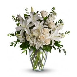 White lilies and cream roses arranged in a clear glass vase
