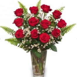 Red roses arranged in a clear glass vase with fern accents