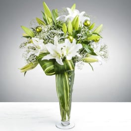 White lilies and green buds arranged in a tall glass vase