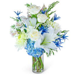 White roses, lilies, and blue hydrangeas in a clear glass vase