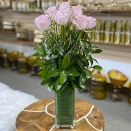 Pink roses arranged in a tall glass vase with dense greenery