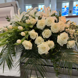 White roses and lilies arranged on a casket with greenery