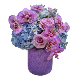 Purple orchids and pink roses arranged with blue hydrangeas in a purple vase