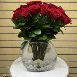 Red roses arranged in a clear round glass vase with white stones.