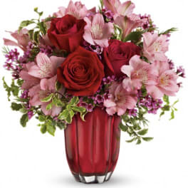 Red roses and pink flowers arranged in a red glass vase