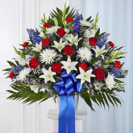 Large standing floral spray with red roses, white lilies, and blue flowers