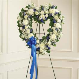 Heart-shaped white and blue floral wreath on a stand with a blue ribbon