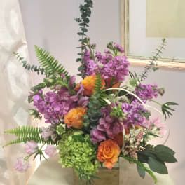 Mixed bouquet with purple flowers and orange roses in a square vase