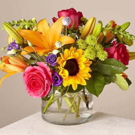 Mixed bouquet of roses, lilies, and a sunflower in a glass vase