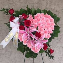 Heart-shaped floral spray with pink carnations, red roses, and lilies on an easel