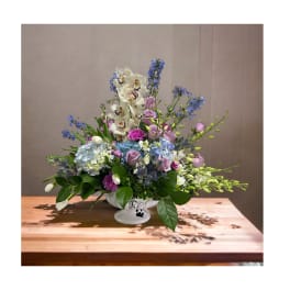Lavender, blue, and white floral arrangement in a white pedestal vase