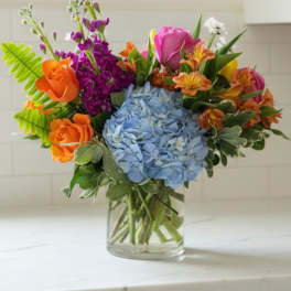 Colorful bouquet with blue hydrangea, orange and pink roses in a glass vase