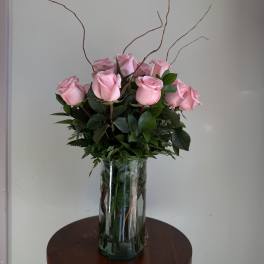 Pink roses arranged in a clear glass vase with tall curly branches