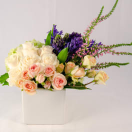 Mixed roses and purple blooms in a white square vase
