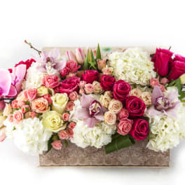 Mixed bouquet of pink roses, orchids, and white hydrangeas in a patterned box